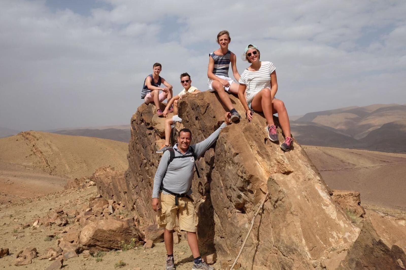 Un grupo de personas sentadas sobre un afloramiento rocoso, con un paisaje montañoso al fondo.