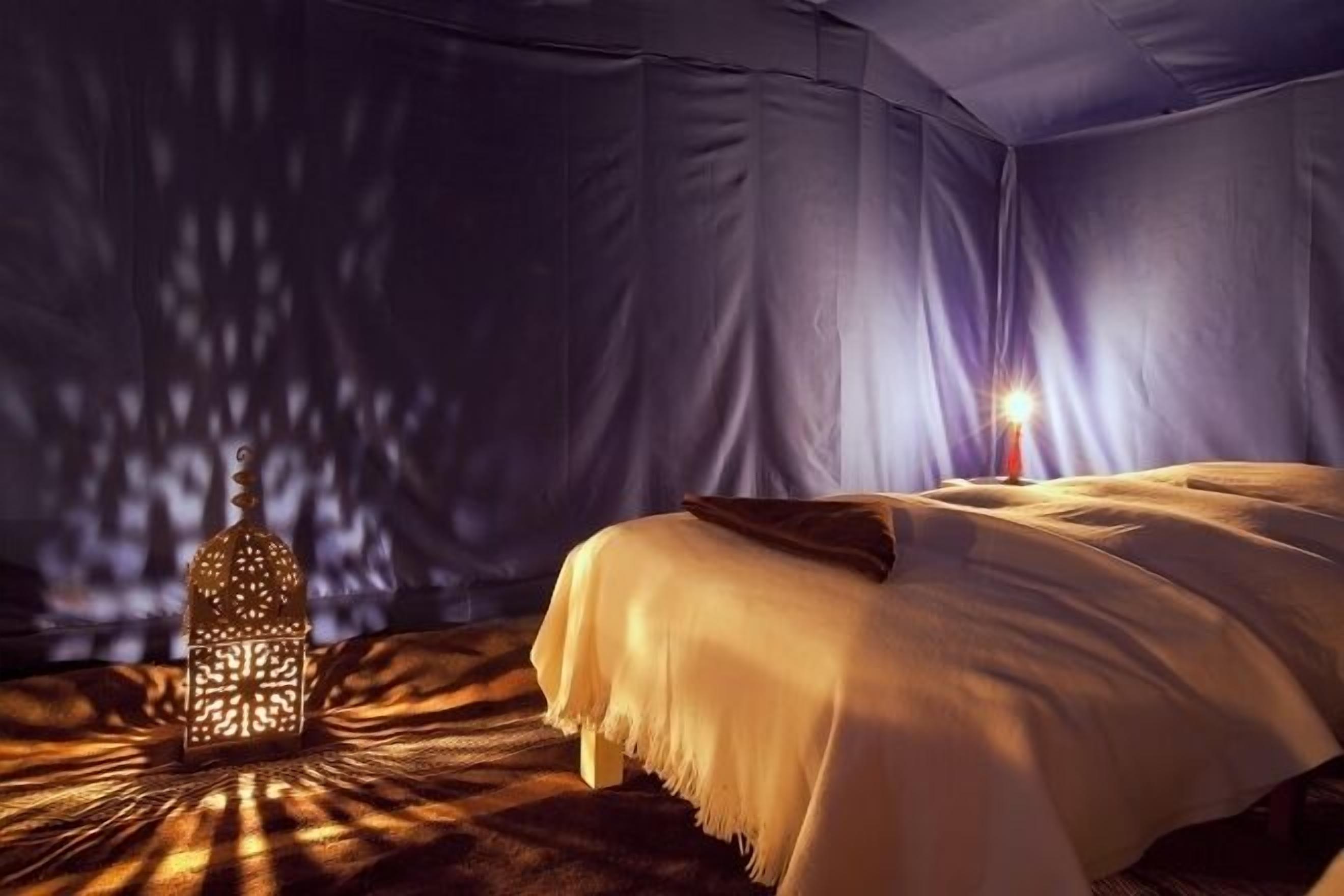 A tented room with a bed, a hanging lantern, and a view of the night sky.