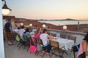 An outdoor dining area with tables and chairs, overlooking a body of water and distant hills. - Ayvalik Palas Hotel (Ayvalik)