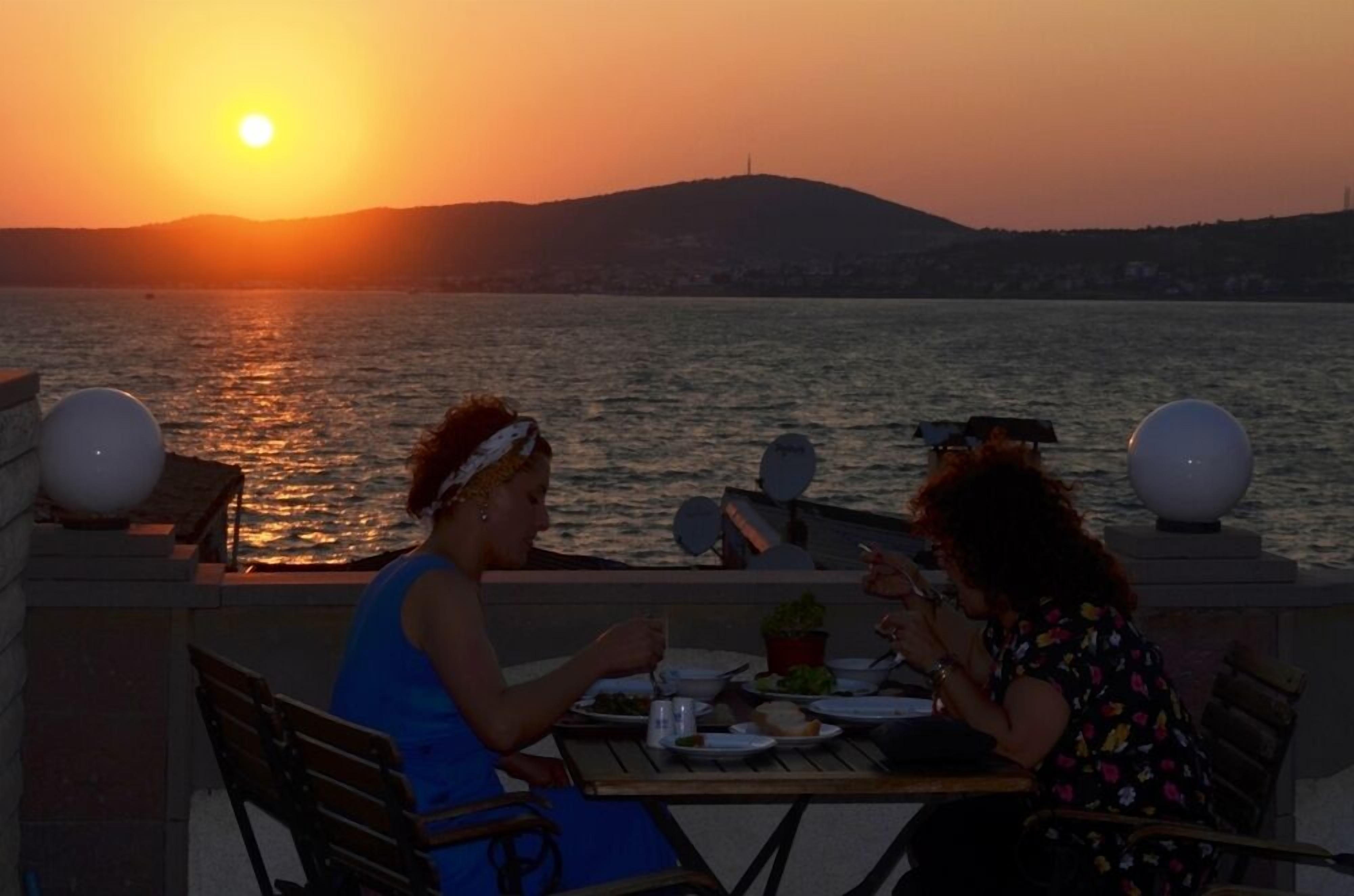 Two people dining at an outdoor table with a view of the sunset over water.