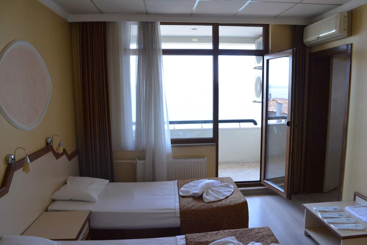 A hotel room with a bed, a bedside table, a window with curtains, and a view of the outside.