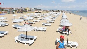 A beach with rows of sun loungers and umbrellas, a clear sky, and a calm sea. - Ayvalik Palas Hotel (Ayvalik)
