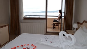 A hotel room with a bed, a view of the sea, a chair, and a table with a lamp. - Ayvalik Palas Hotel (Ayvalik)