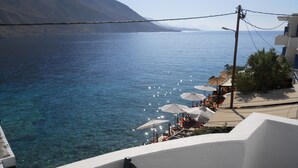 A coastal view with clear blue sea, a mountain in the background, and outdoor seating with umbrellas. - Daskalogiannis Hotel (Sfakia)
