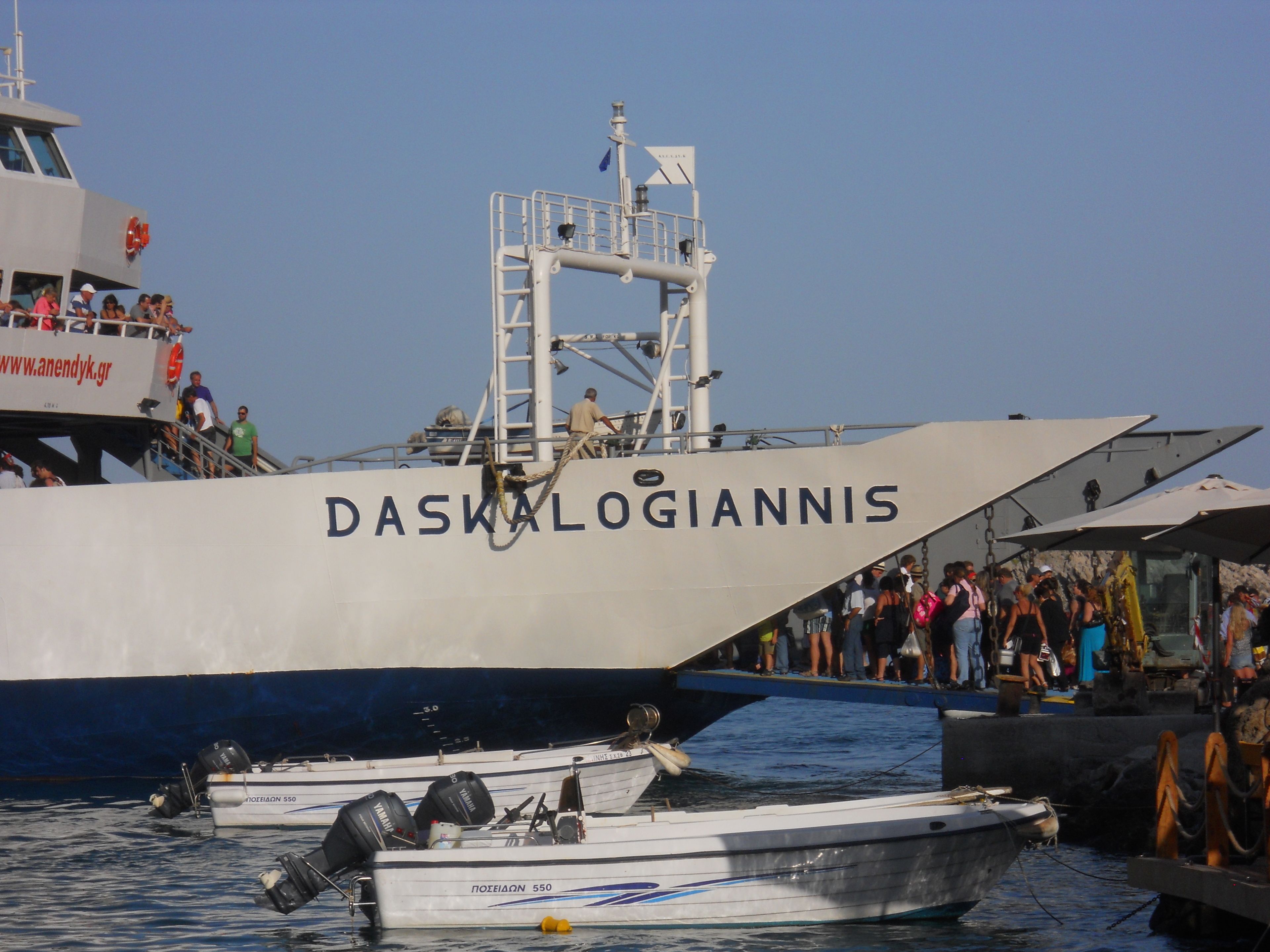 Un grand bateau, le « DASKALOGIANNIS », a accosté dans un port. Il y avait des personnes à bord et de plus petits bateaux étaient amarrés à proximité.