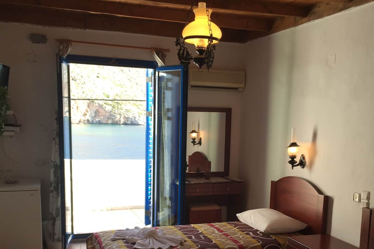 A room with two beds, a wooden ceiling, a door leading outside, and a wall-mounted light fixture.