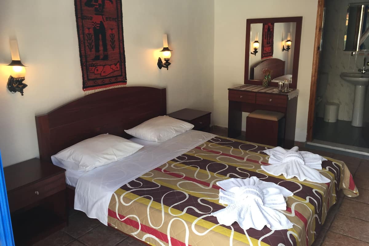 A hotel room with a bed, bedside tables, a dresser, a mirror, and a bathroom visible through an open door.