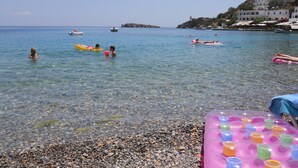 A pebbled beach with clear water, boats, and people swimming. - Daskalogiannis Hotel (Sfakia)