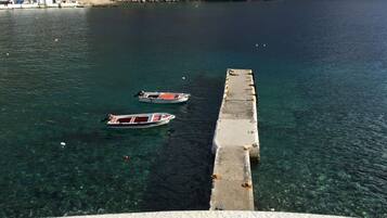 A pier extending into a clear blue sea with two boats moored at the end.