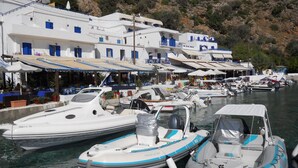 A marina with several boats docked, surrounded by white buildings with blue accents and outdoor seating areas. - Daskalogiannis Hotel (Sfakia)