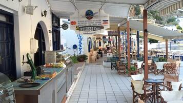 An outdoor cafe area with tables and chairs, a food display, and a sign for the Jasiaklogianni's Hotel.