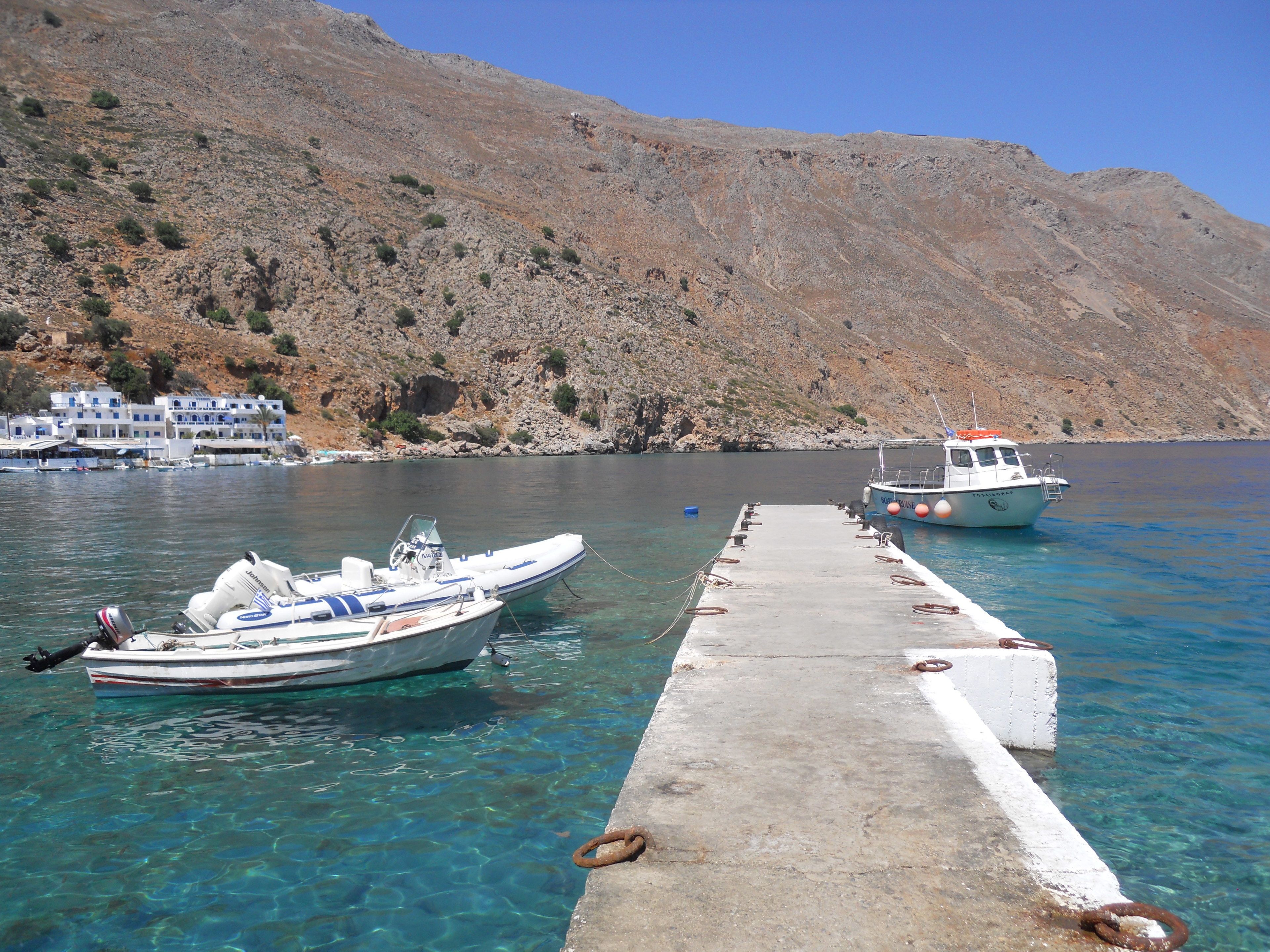 A boat docked at a pier with clear water and a mountainous backdrop.