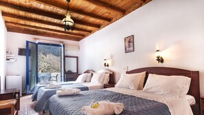 A hotel room with two beds, wooden ceiling beams, a balcony with a mountain view, and a small table with chairs. - Daskalogiannis Hotel (Sfakia)