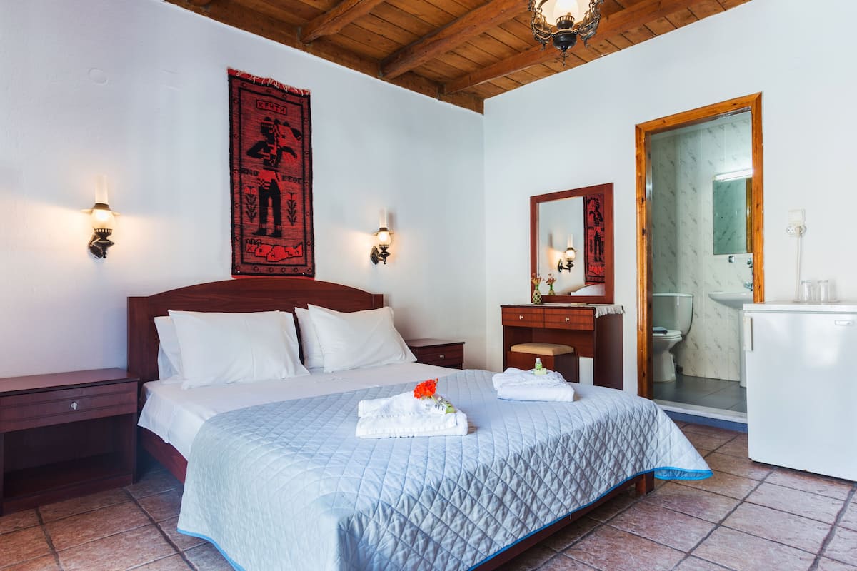 A hotel room with a large bed, wooden headboard, two nightstands, a dresser, a mirror, and a bathroom visible through an open door.