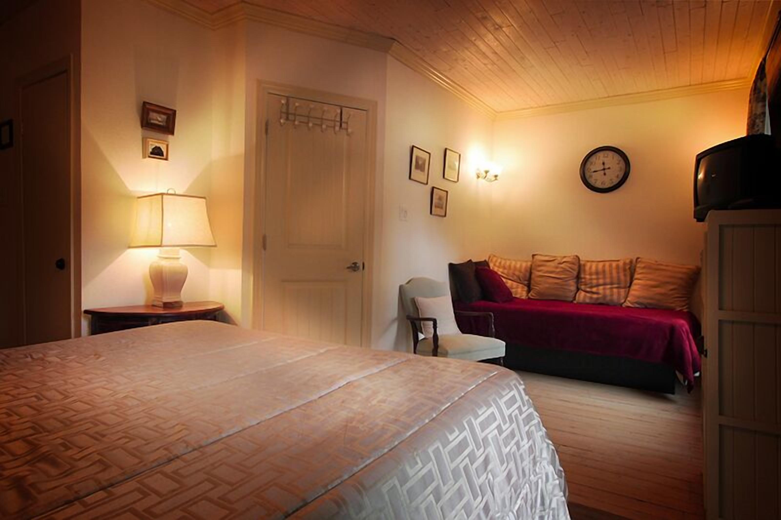 A bedroom with a bed, a chair, a sofa, a lamp, a clock, and a television.