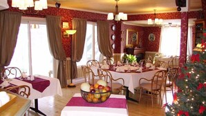 Un comedor con mesas redondas dispuestas para una comida, un frutero sobre la mesa y un árbol de Navidad en la esquina.