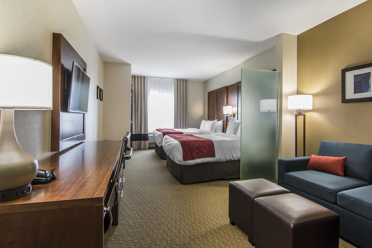 A hotel room with a wooden desk, a bed with a red blanket, a blue sofa, and a large mirror.