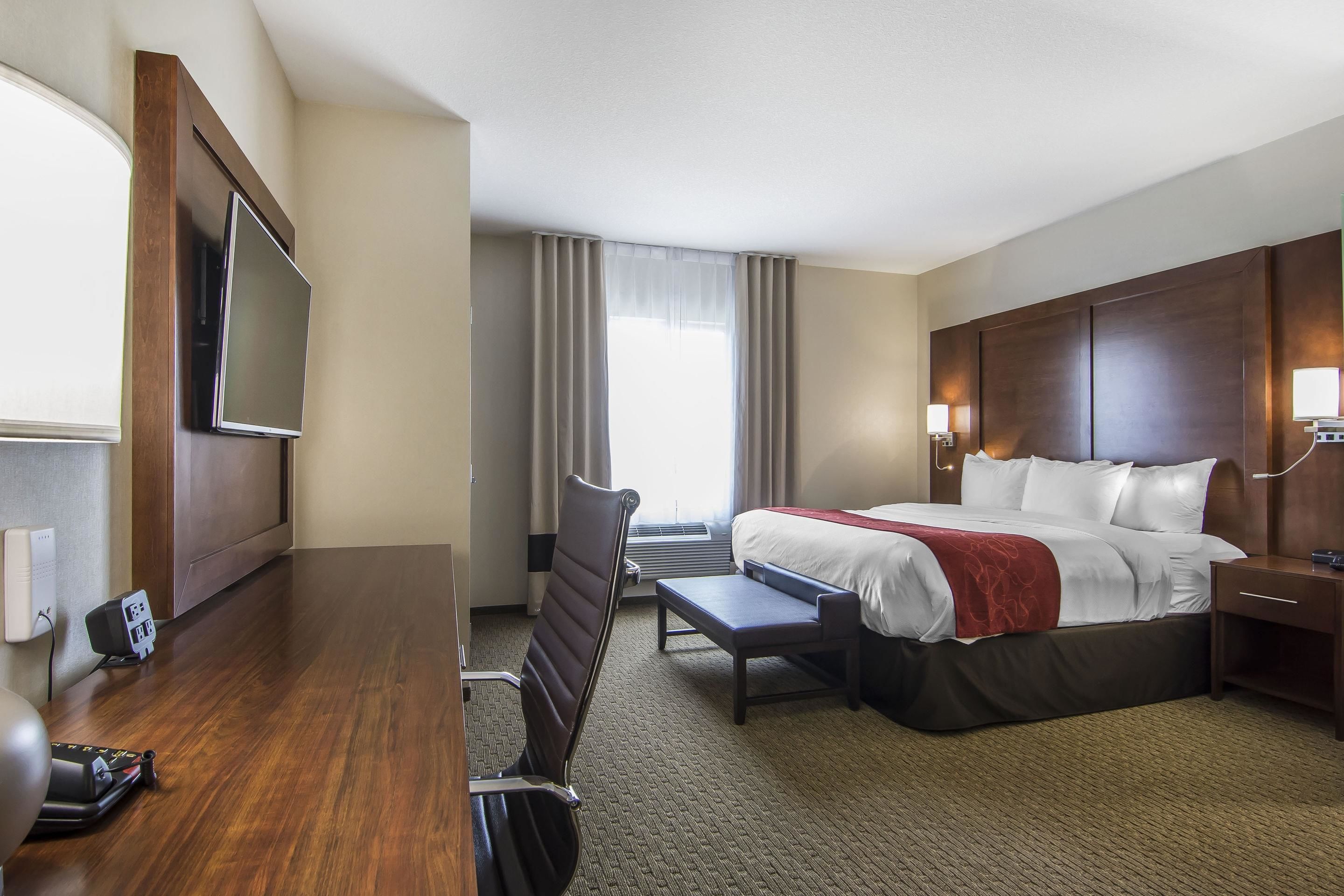 Een hotelkamer met een bed, nachtkastje, stoel, bureau, televisie en een raam met gordijnen.