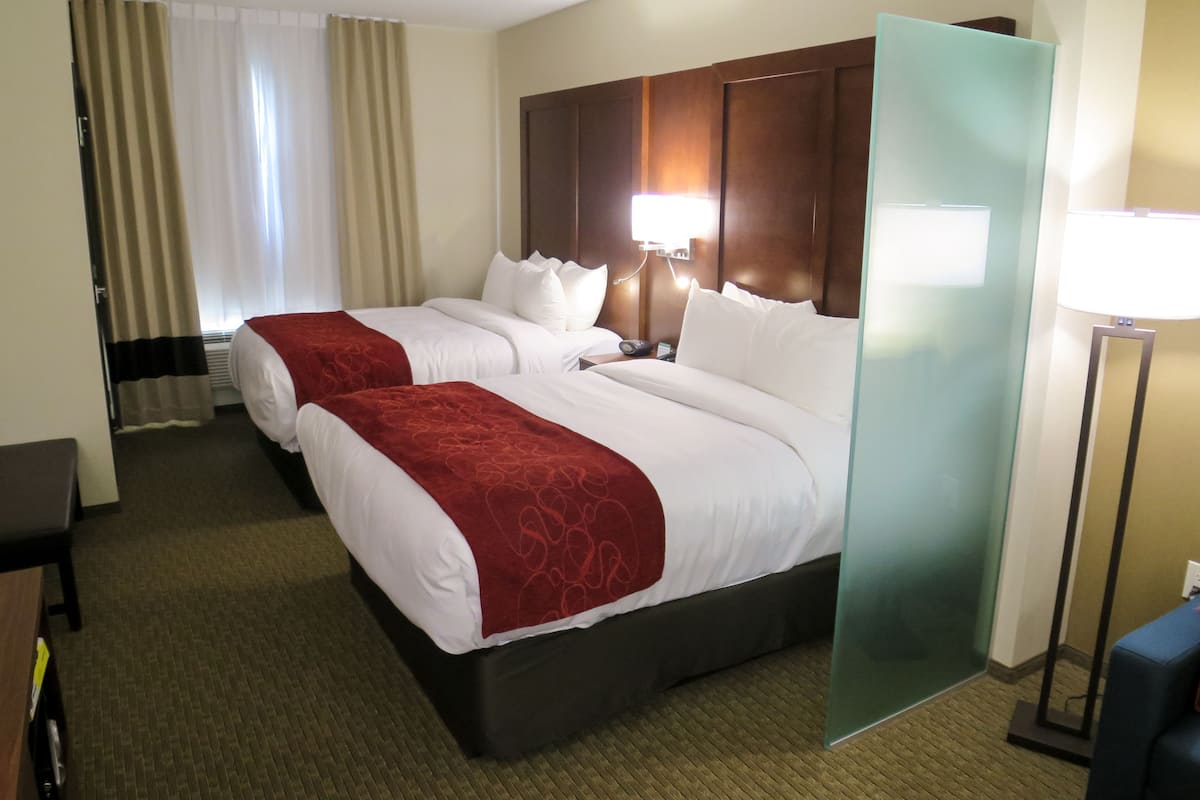 A hotel room with two beds, a desk, a chair, a lamp, and a large mirror.