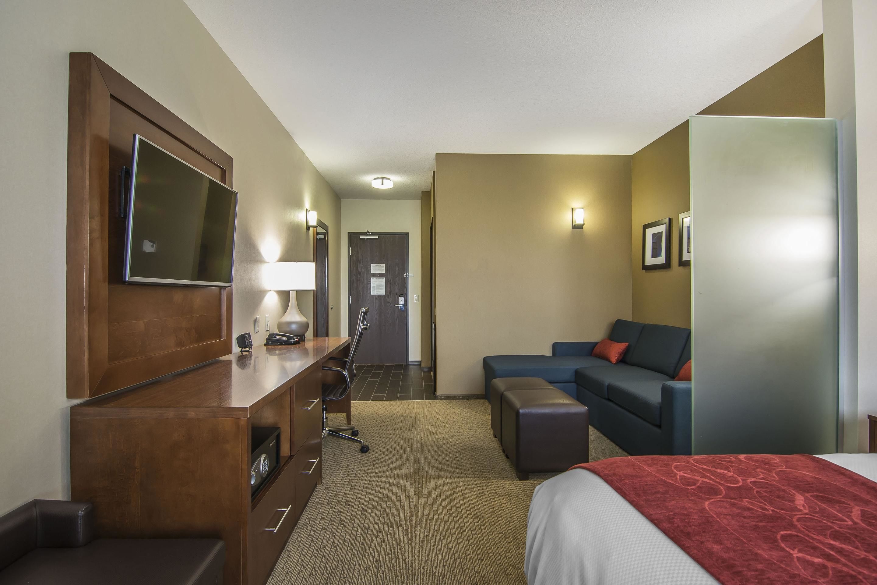 Habitación de hotel con cama, escritorio con silla, sofá, televisor montado en la pared y puerta que da a otra habitación.