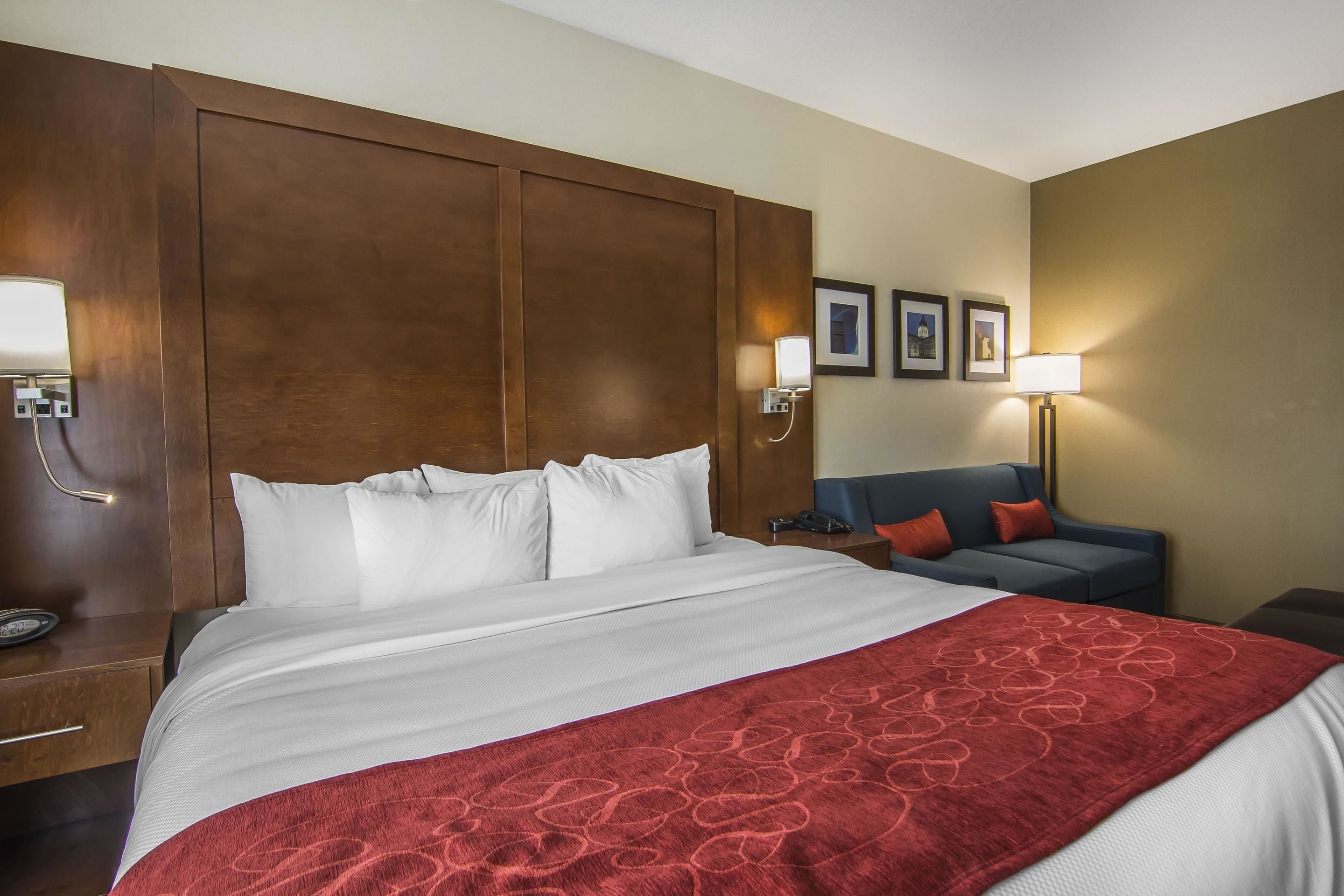 A hotel room with a large bed, a blue sofa, a wooden headboard, and a red throw blanket.