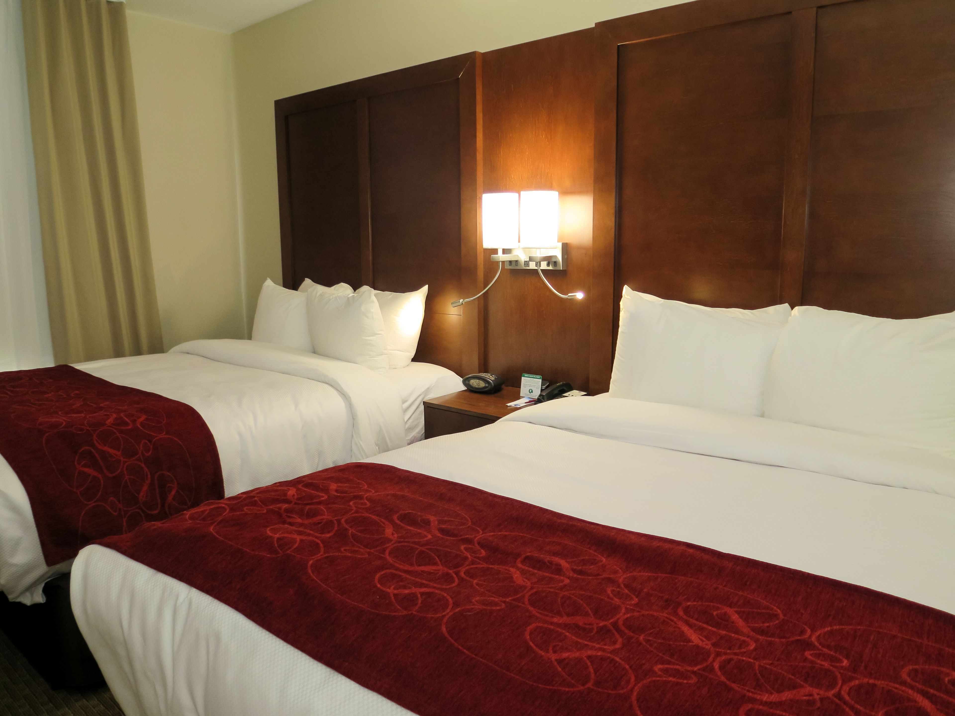 A hotel room with two beds, a wooden headboard, a bedside table with a lamp, and a telephone.
