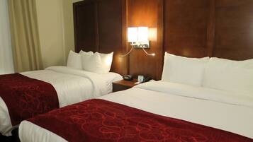 A hotel room with two beds, a wooden headboard, a bedside table with a lamp, and a telephone.