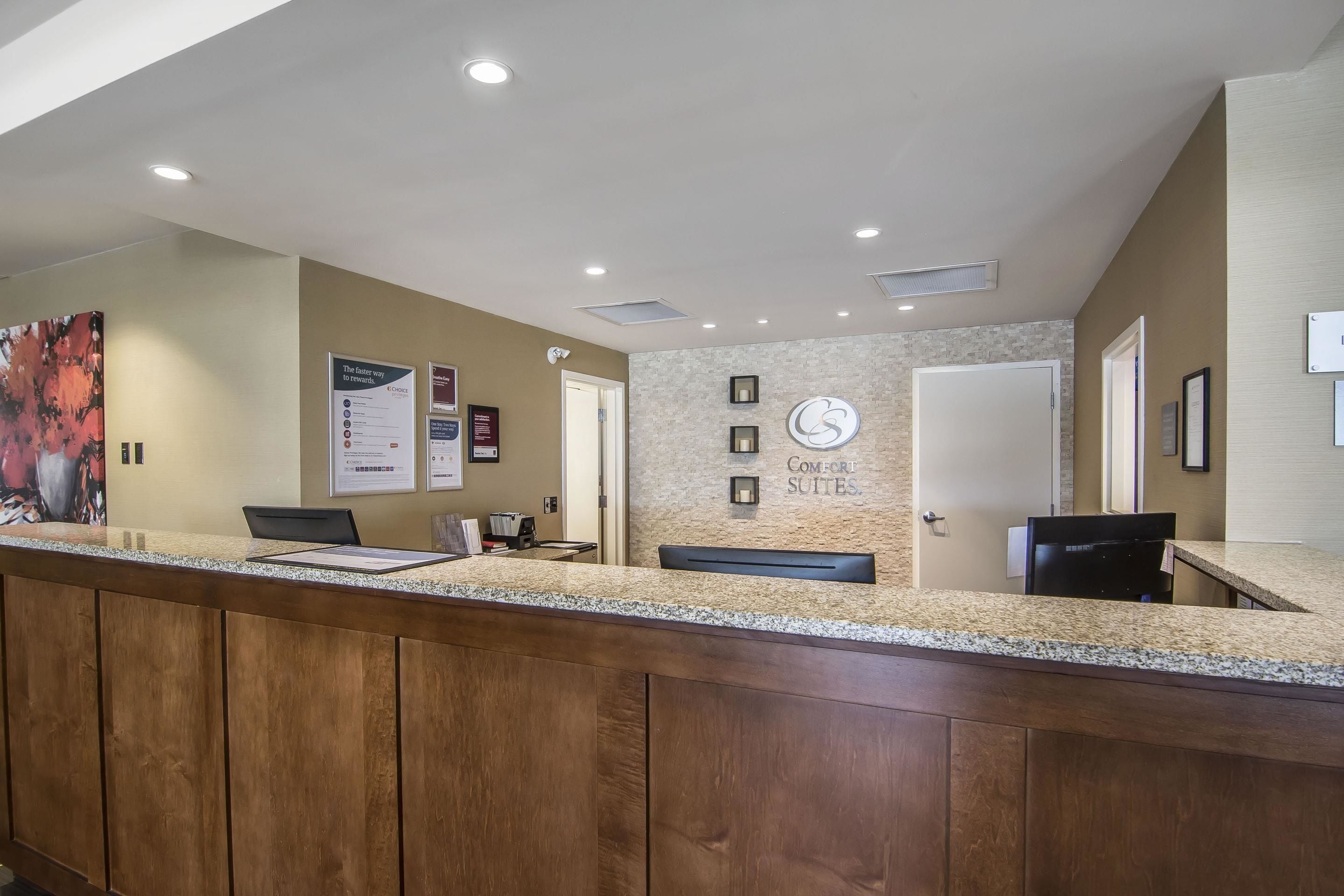 A reception area with a wooden counter, a clock, and a wall with 'COMFORT SUITES' signage.