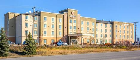 A multi-story hotel with a central entrance, multiple windows, and a parking lot in front.