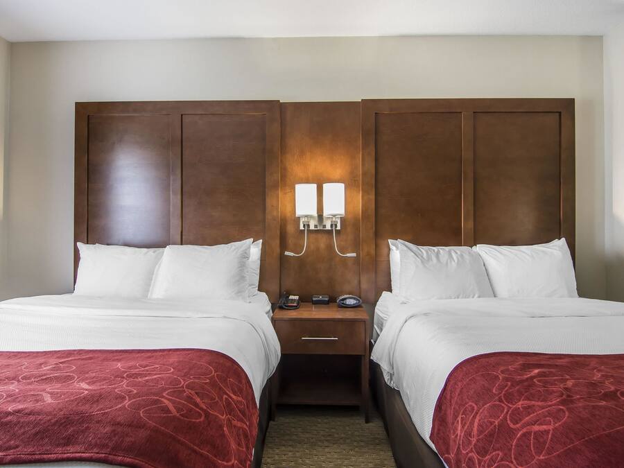 A double room with two beds, a wooden headboard, bedside tables with lamps, and a carpeted floor.