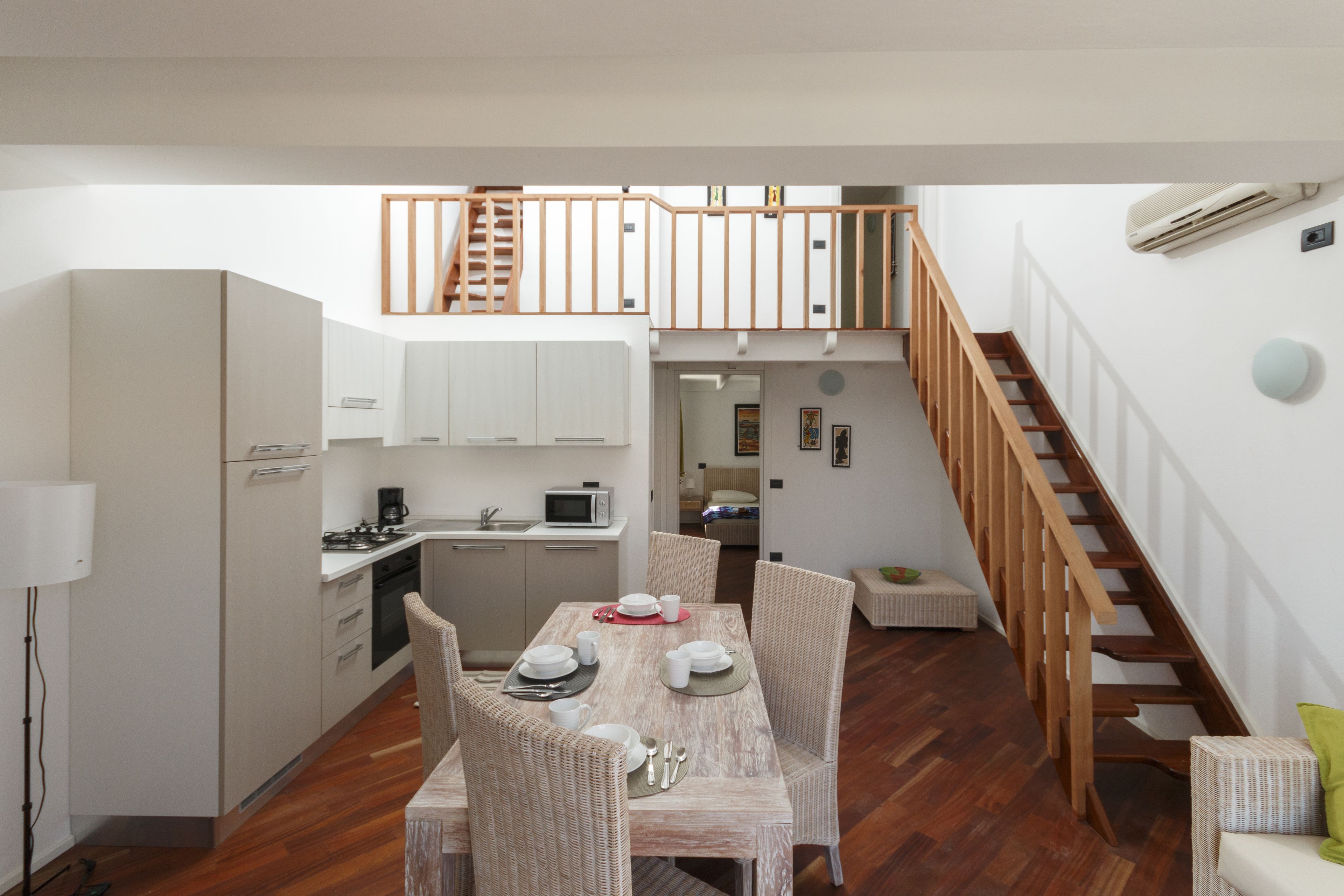 Una cocina moderna con armarios blancos, una mesa de comedor preparada para cuatro personas y una escalera de madera que sube a un nivel superior.