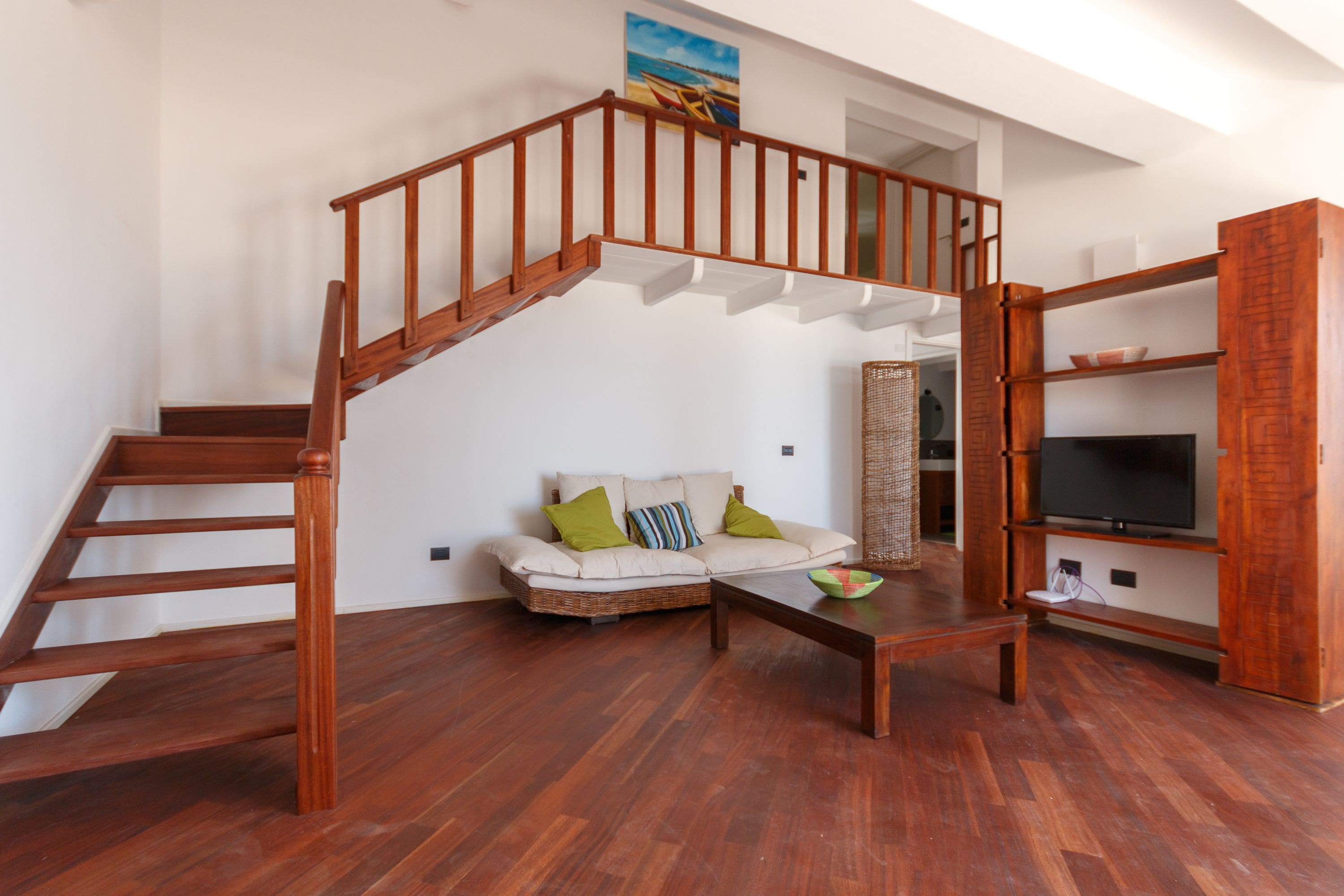 A spacious living area with a wooden staircase, a sofa with cushions, a coffee table, and a TV stand.
