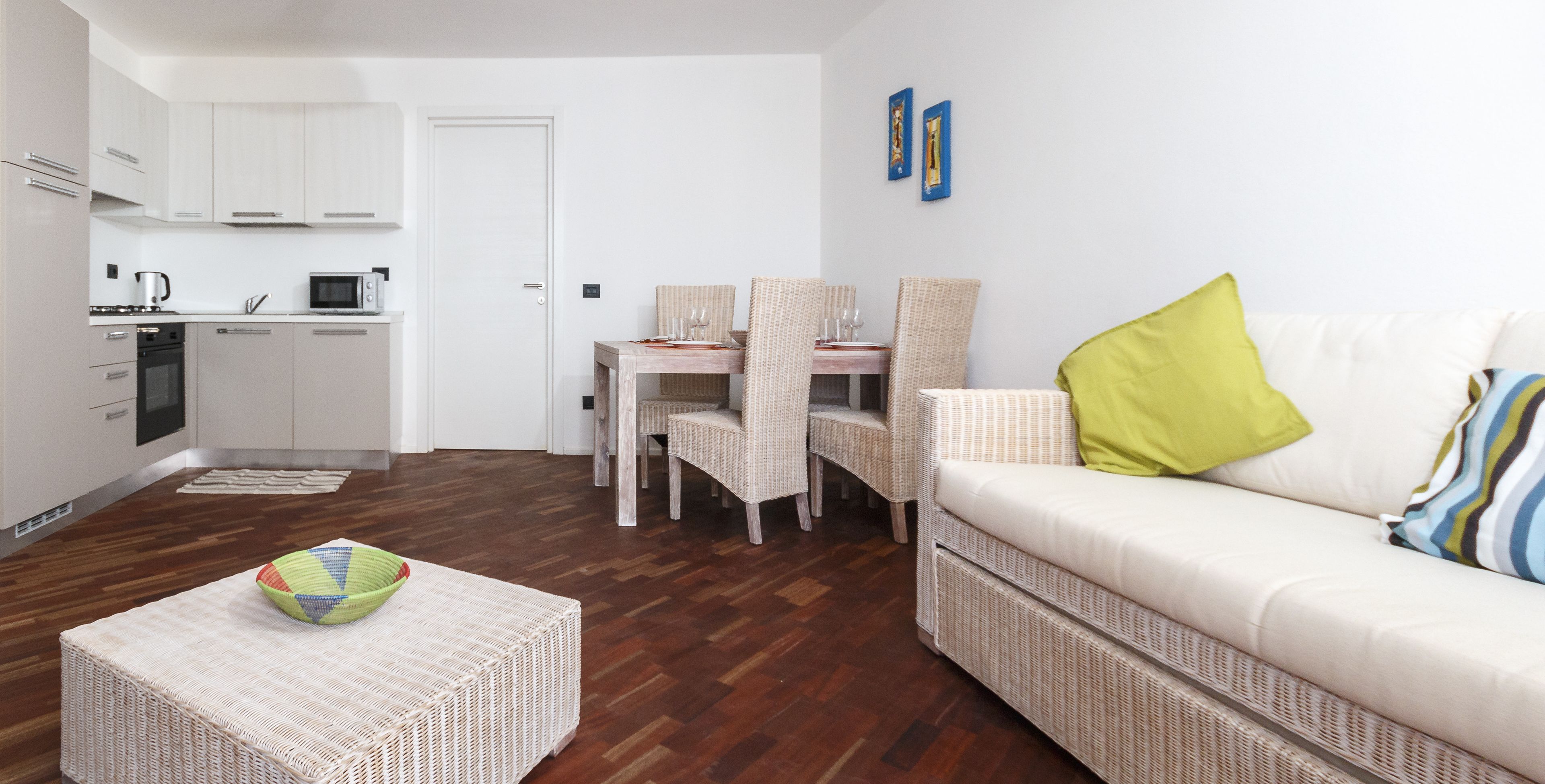 A modern living room with a white sofa, wicker furniture, and a dining area with wicker chairs and a table.