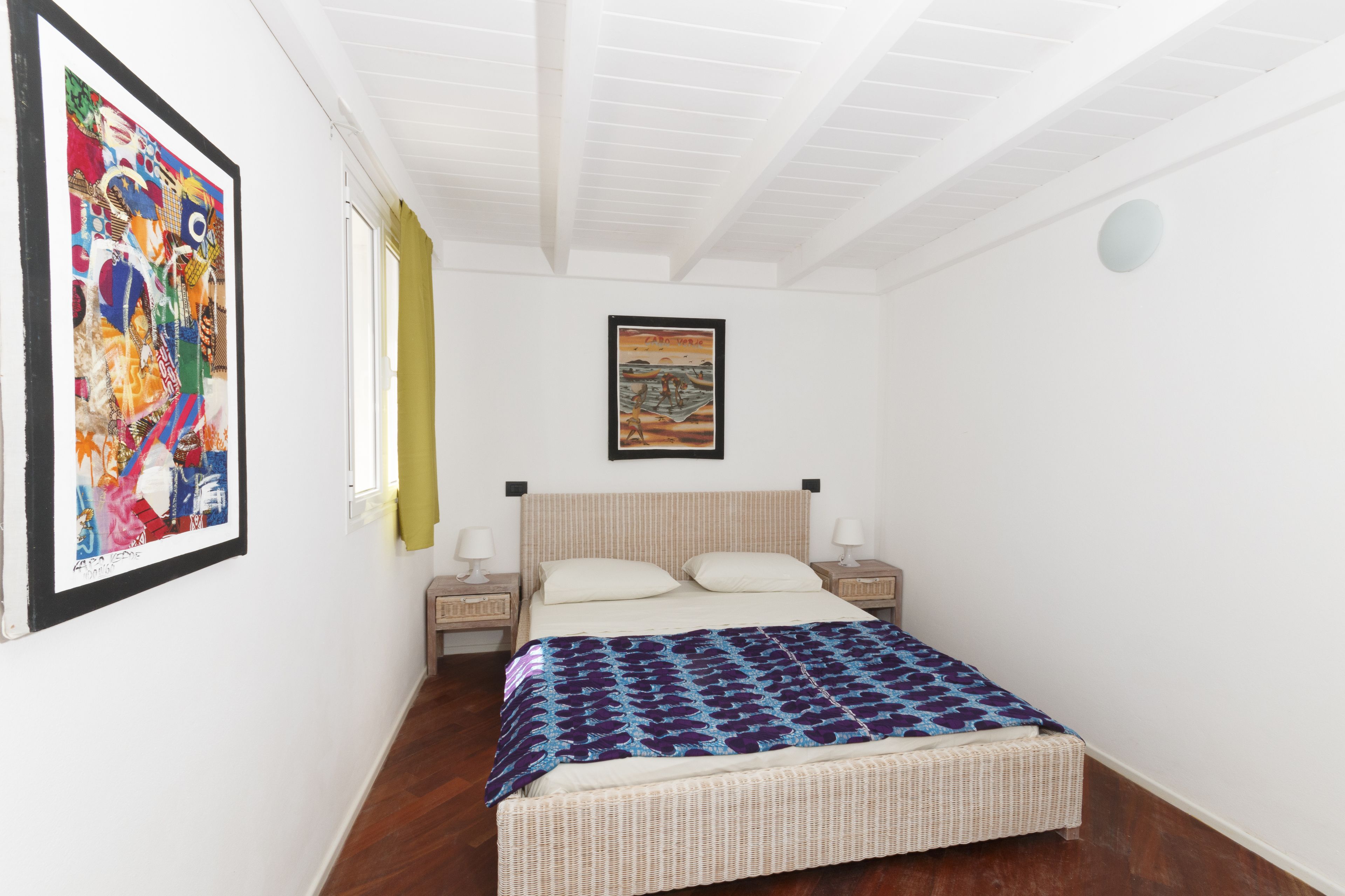 A bedroom with a bed, two bedside tables, a window, and a painting on the wall.