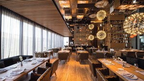 Un restaurant modern amb taules comunitàries llargues, llums esfèriques penjants i un sostre de fusta.