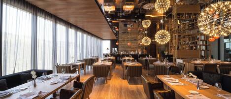 Un restaurant moderne avec de longues tables communes, des luminaires sphériques suspendus et un plafond en bois.