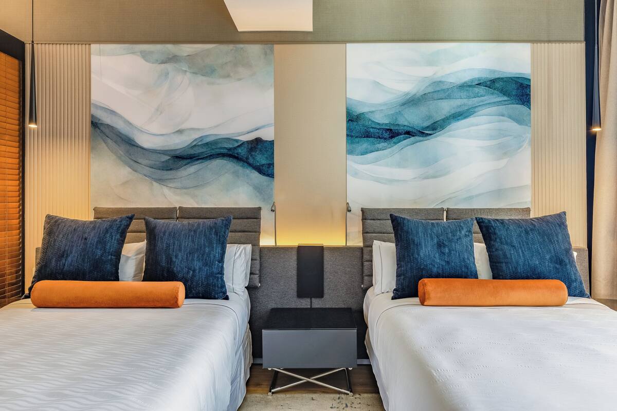 Habitación de hotel con dos camas, una mesita de noche y arte abstracto en la pared.