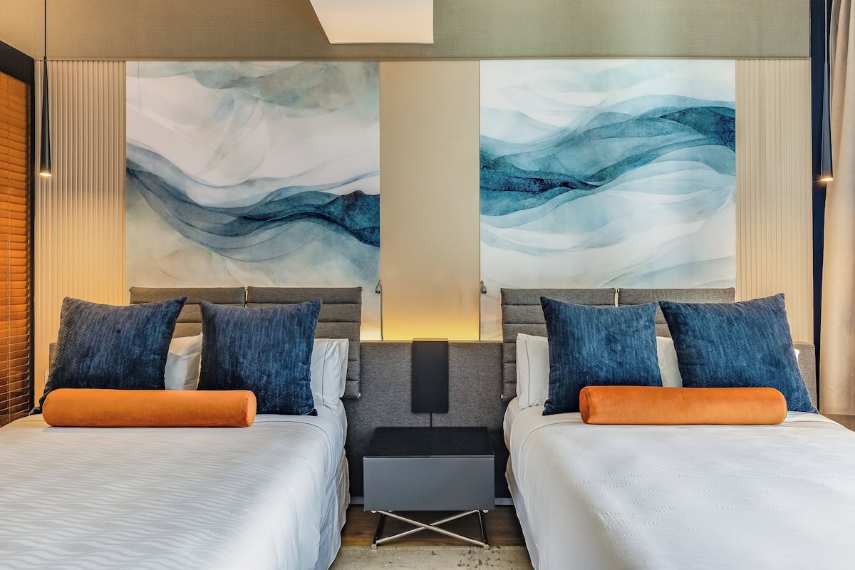 A hotel room with two beds, a nightstand, and abstract wall art.