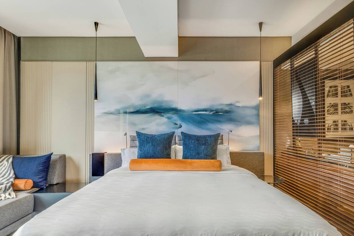 Una habitación de hotel moderna con una cama grande, un sofá y un cuadro abstracto de gran tamaño en la pared.