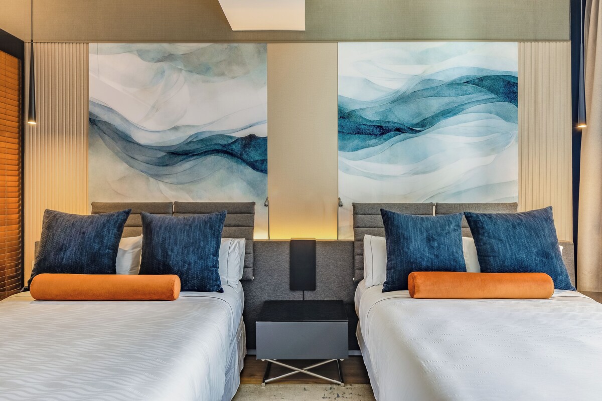 Habitación de hotel con dos camas, una mesita de noche y arte abstracto en la pared.