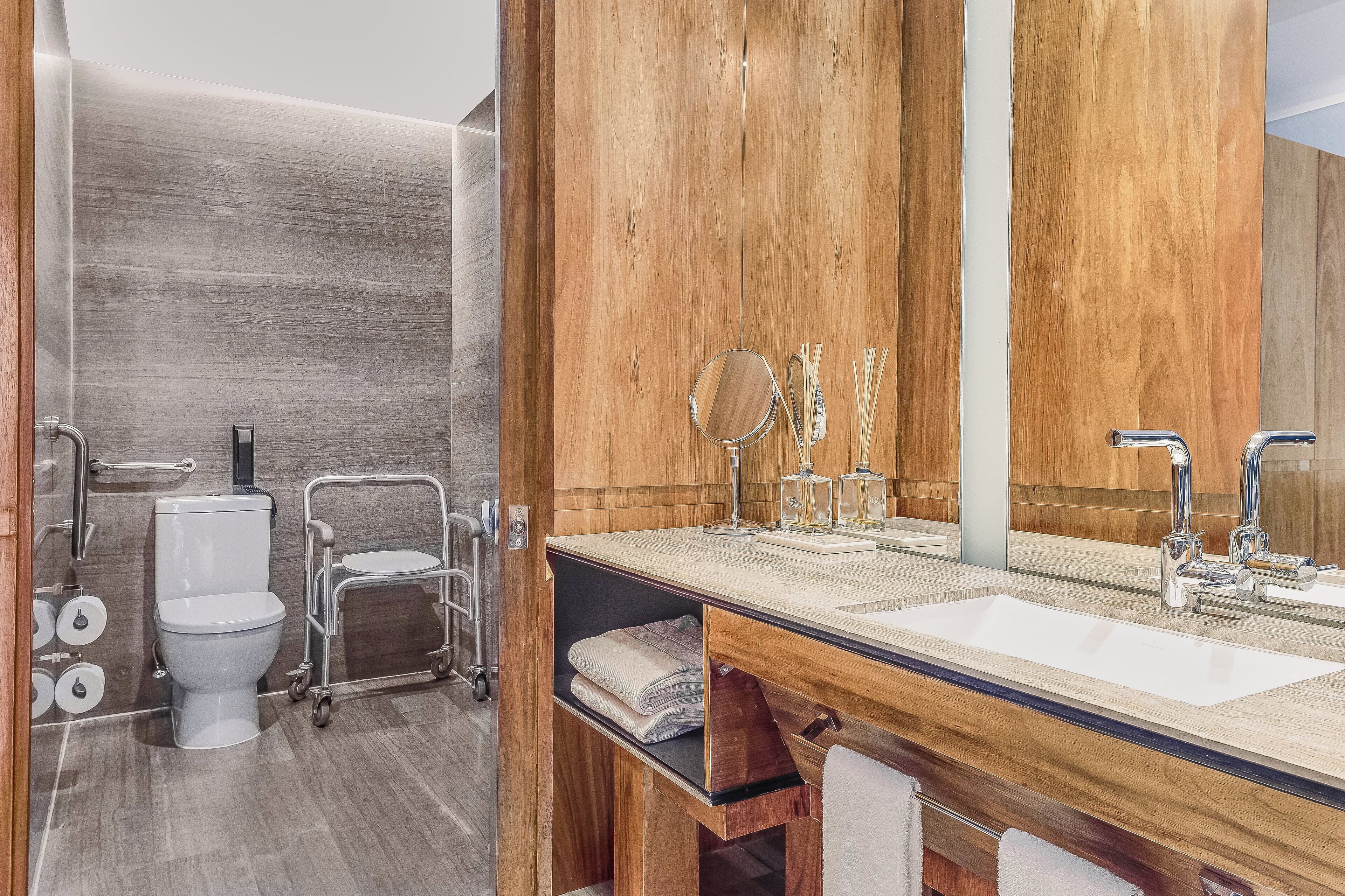 A modern bathroom with a wooden vanity, a large mirror, and a toilet with a wheelchair-accessible cart.