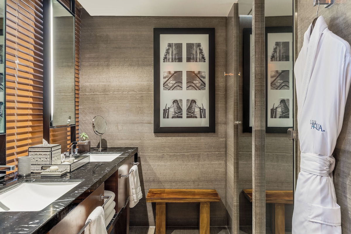 Une salle de bain moderne avec un meuble-lavabo en bois, un grand miroir et un tableau encadré représentant un pont.