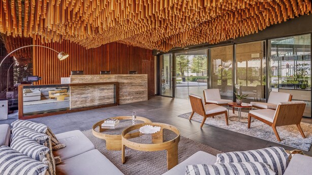 Un espace d’accueil moderne doté d’un plafond en bois, d’un comptoir de réception et de différents espaces d’assise.