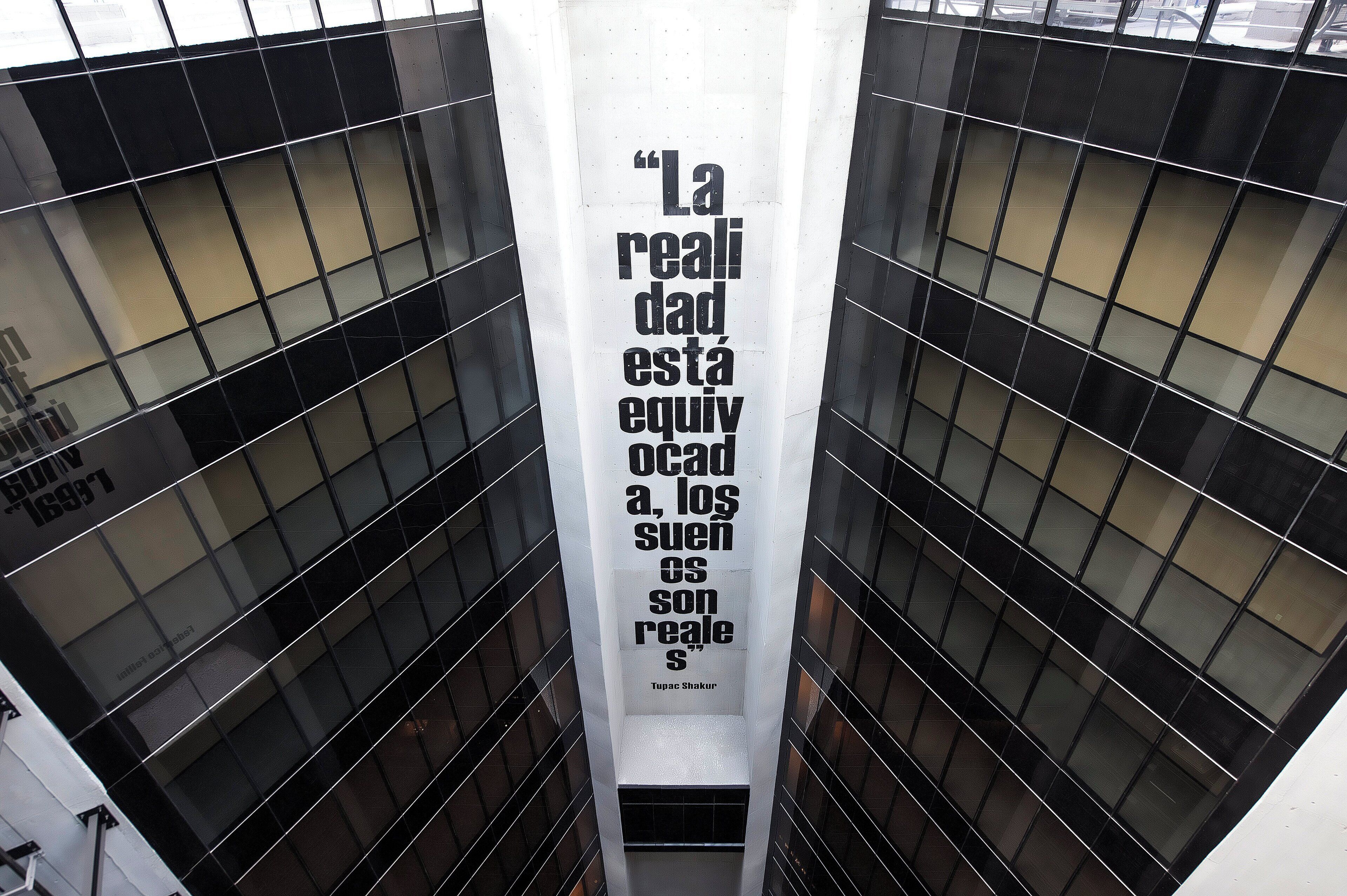 A tall building with a reflective glass facade and a vertical sign with text.