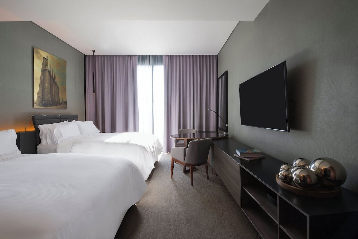 Habitación de hotel con cama, escritorio, silla, televisor de pantalla plana y un cuadro en la pared.