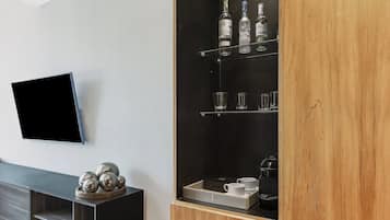 Ein modernes Wohnzimmer mit einem flachbildfernseher an der Wand, einer Holzkabine mit Regalen für Flaschen und Gläser sowie einer dekorativen Metallskulptur auf einem Konsolentisch.