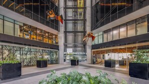 Un bâtiment moderne doté de grandes fenêtres en verre, d’un atrium central et de jardinières noires ornées de plantes vertes.