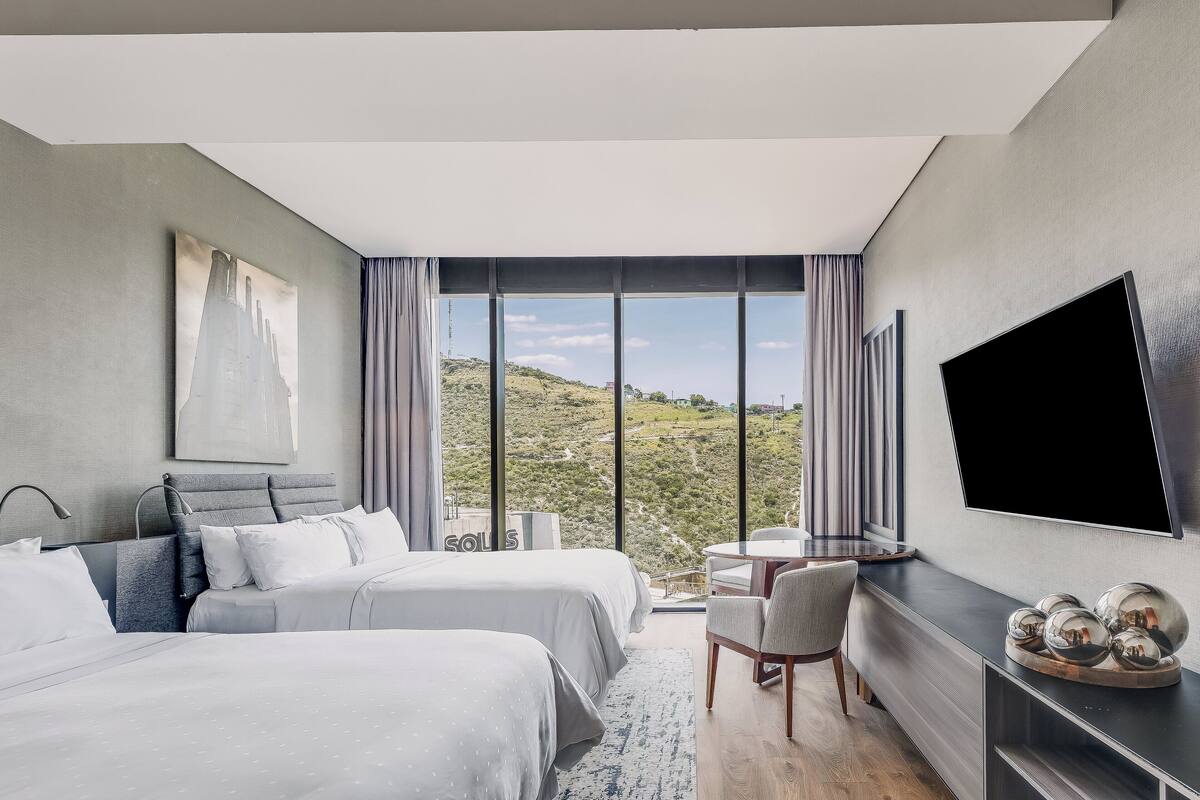 Una habitación de hotel moderna con dos camas, un televisor grande y vistas panorámicas.