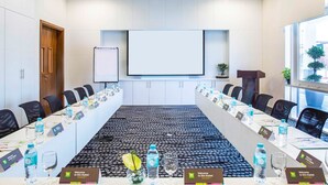 Een vergaderruimte met een lange tafel, stoelen, een projectiescherm en een groot raam.