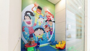 Een kinderspeelruimte met kleurrijk speelgoed en een muurschildering van stripfiguren.